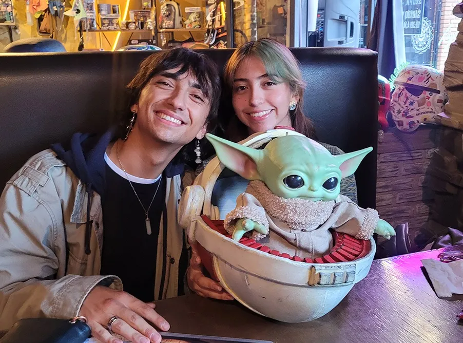 Pareja sentada a la mesa con Grogu en su cuna